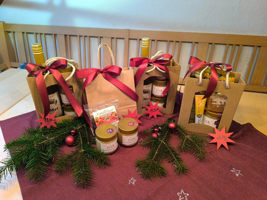 Weihnachtliche Geschenktüten mit Honig, Met und weiteren Bienenprodukten, dekoriert mit roten Schleifen und Tannenzweigen.
